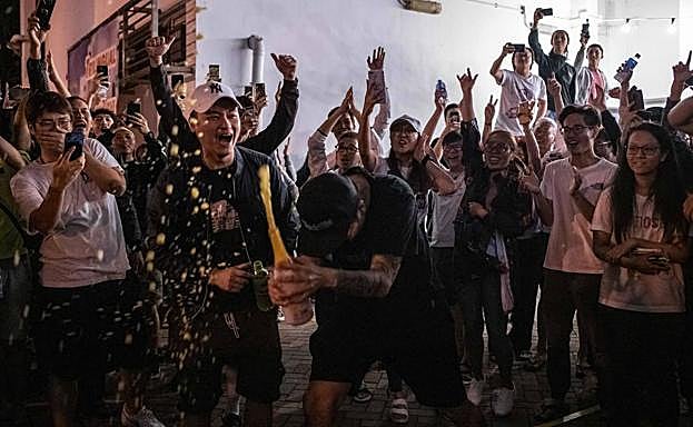 Manifestantes prodemocracia celebran con champán los resultados de los comicios locales junto a un colegio electoral.