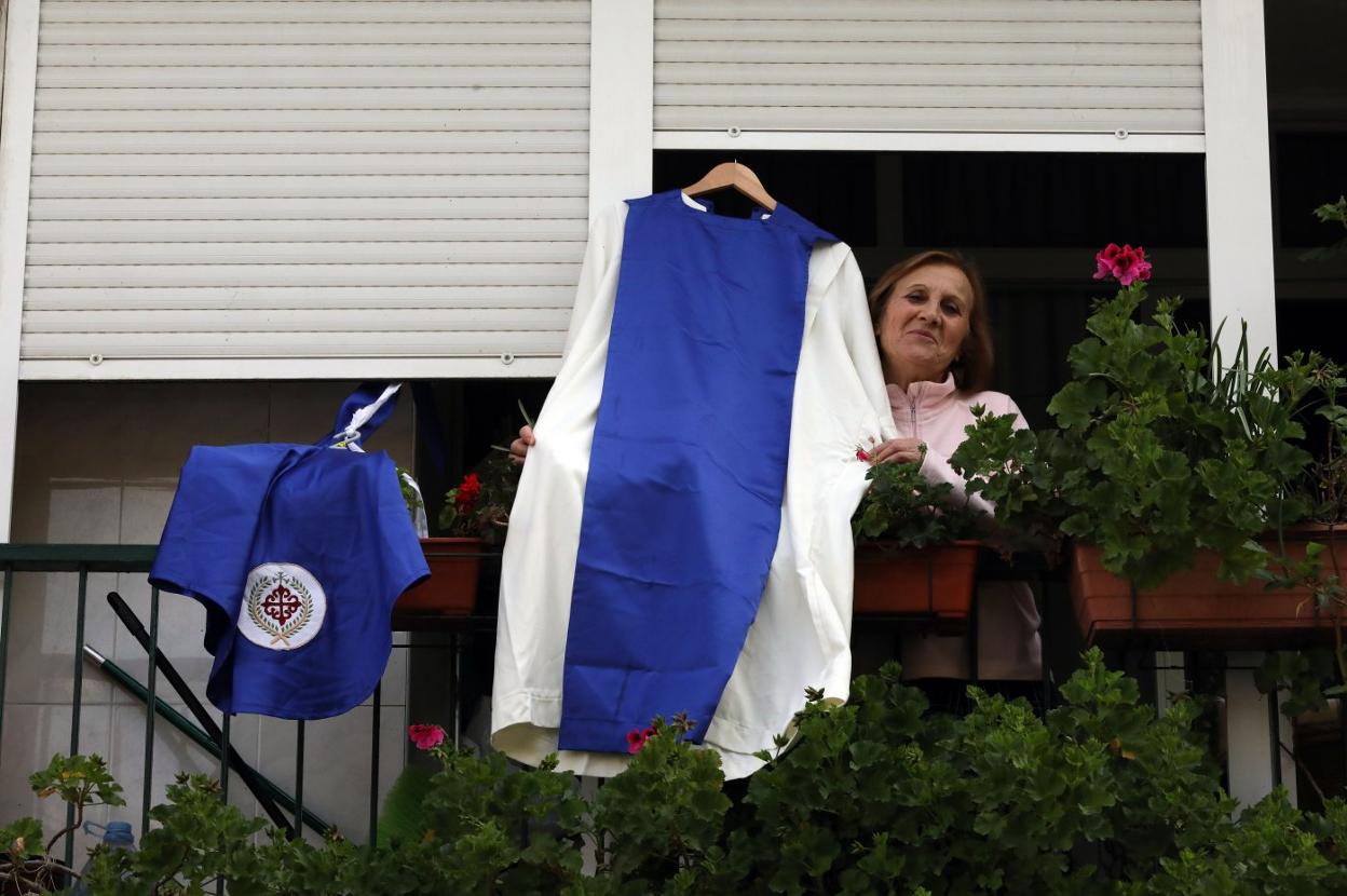 Una mujer muestra un traje de nazareno desde su balcón. 