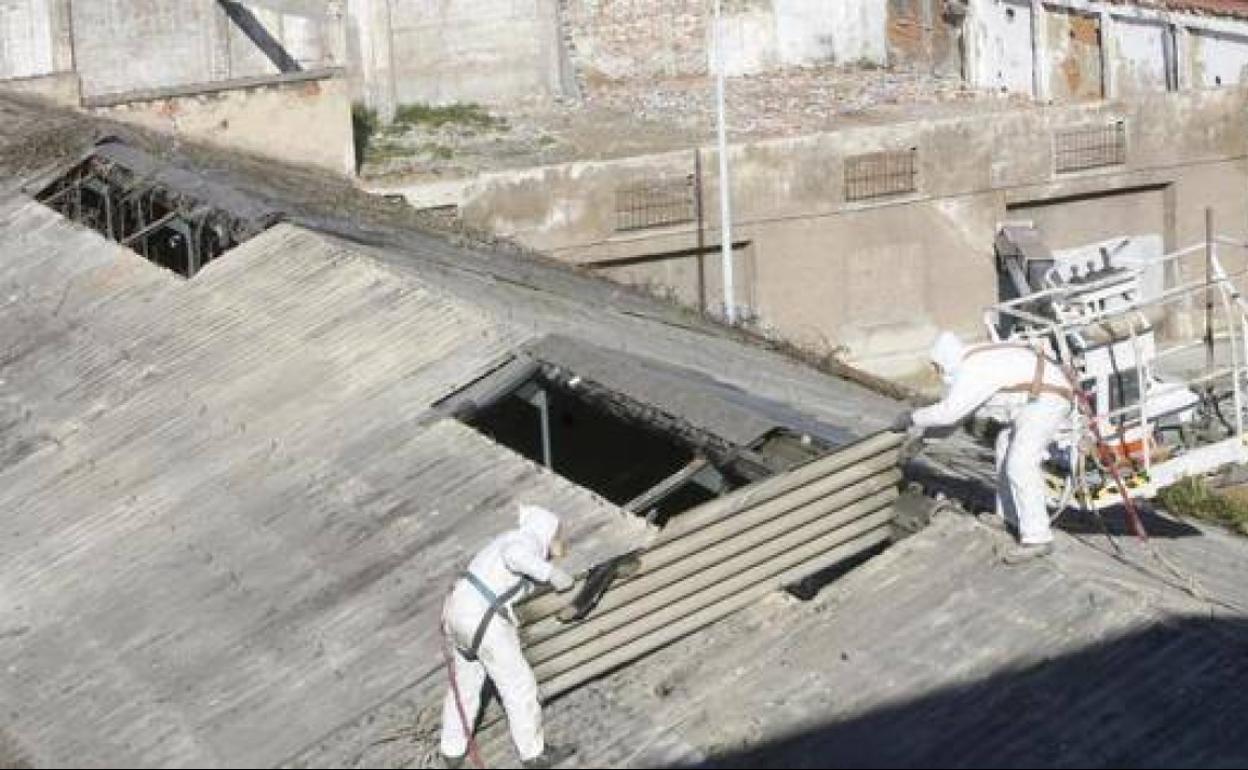 Dos de los operarios retiran los techos. de amianto.