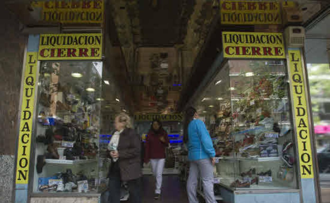 Clientas ante el escaparate de una zapateria en liquidación por cierre 