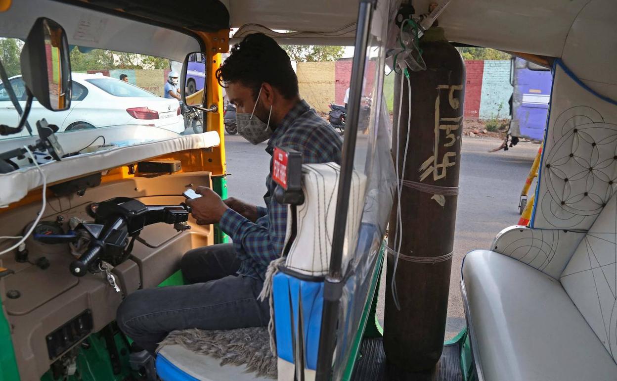 Khan consulta el móvil en su tuk-tuk medicalizado, con la bombona de oxígeno para el paciente.