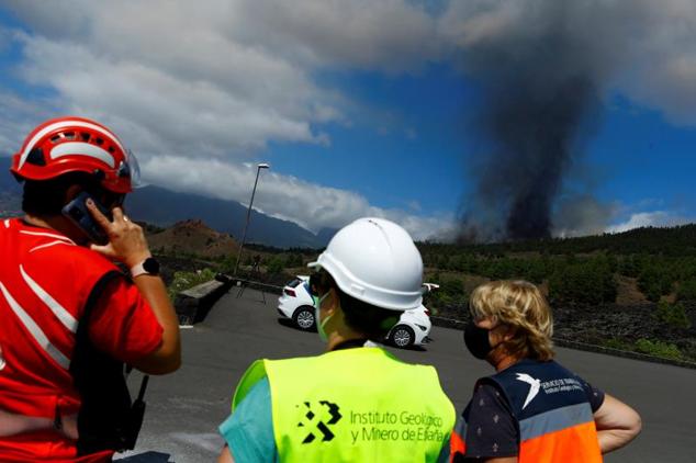 Tres persnas observan la columna de humo que se eleva tras la erupción del volcán.