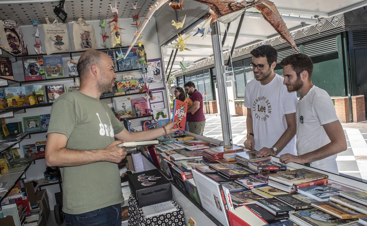 Agustín Lozano de la librería Tusitala recomenando un libro a dos lectores en la feria de Badajoz. 