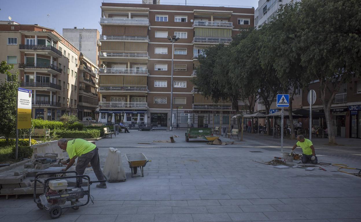 Dos operarios dándole los últimos remates al nuevo suelo de la plaza de los Alféreces. 