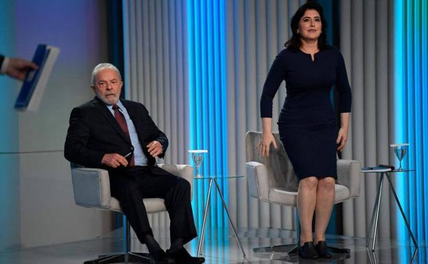 Tebet se dispone a tomar asiento antes de un debate televisivo electoral, junto al exmandatario Lula.