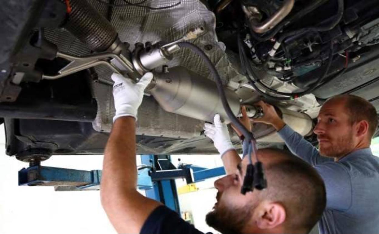 Dos técnicos manipulan el catalizador de un vehículo.