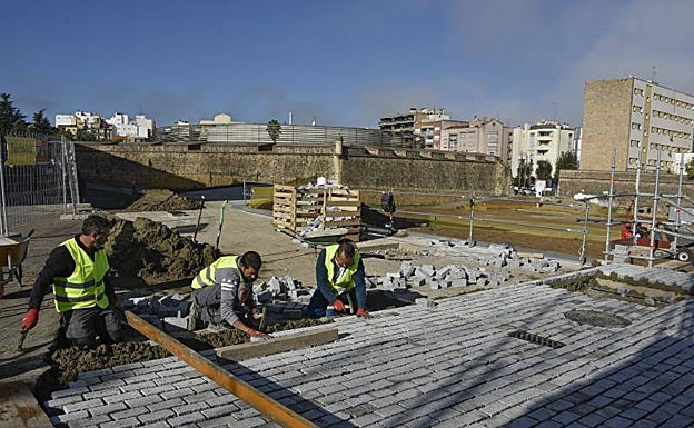 Operarios colocan el pavimento en la calle Stadium y, por detrás, se ve la muralla despejada. 
