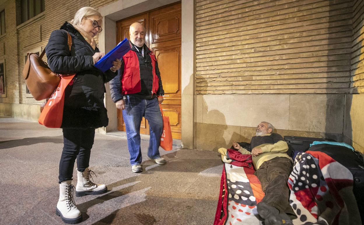 Un coordinador de la Cruz Roja y una voluntaria hacen una encuesta a una persona que pasa la noche bajo los porches de la Plaza del Pilar de Zaragoza