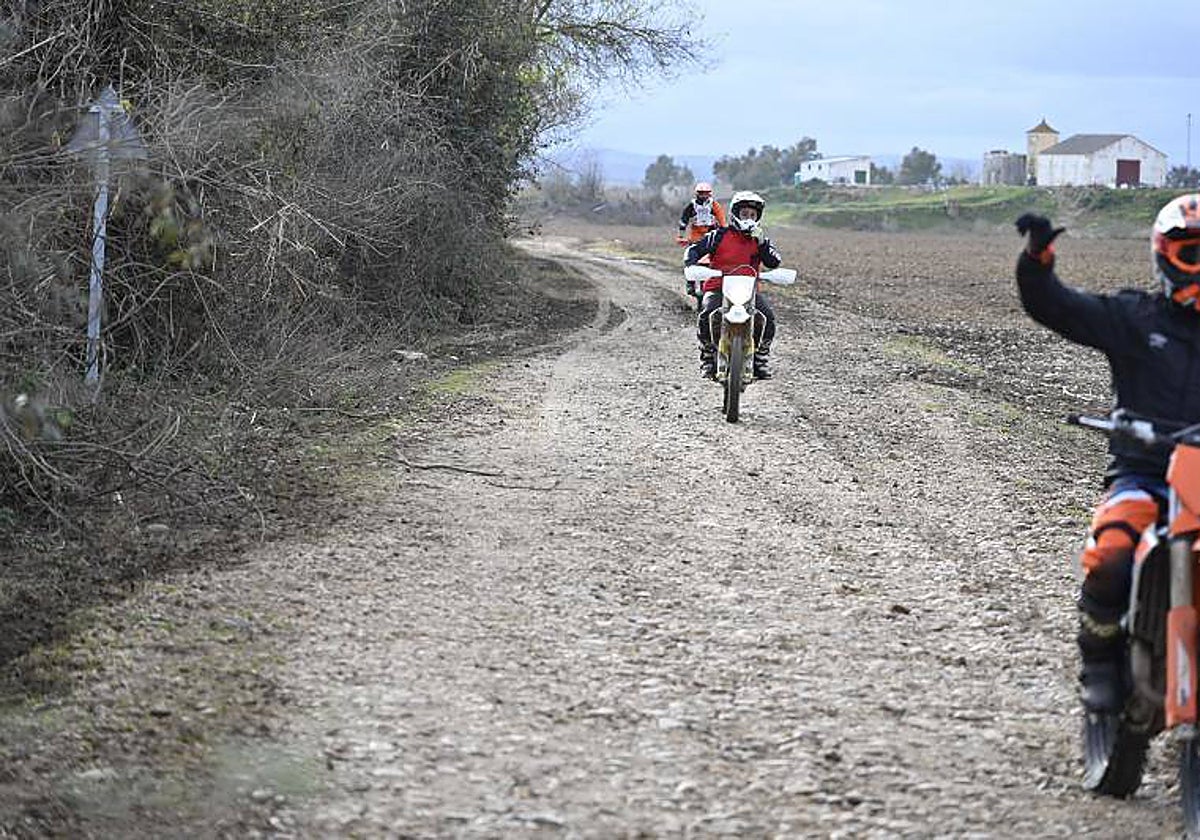 Tres motoristas circulan por la pista que conecta el Puente Real con la pasarela, que está llena de piedras y socavones.