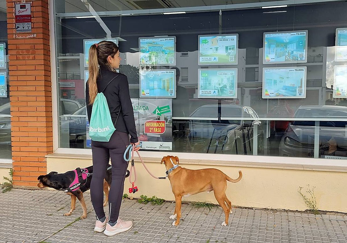 Una joven ante el escaparate de una inmobiliaria con anuncios de viviendas.