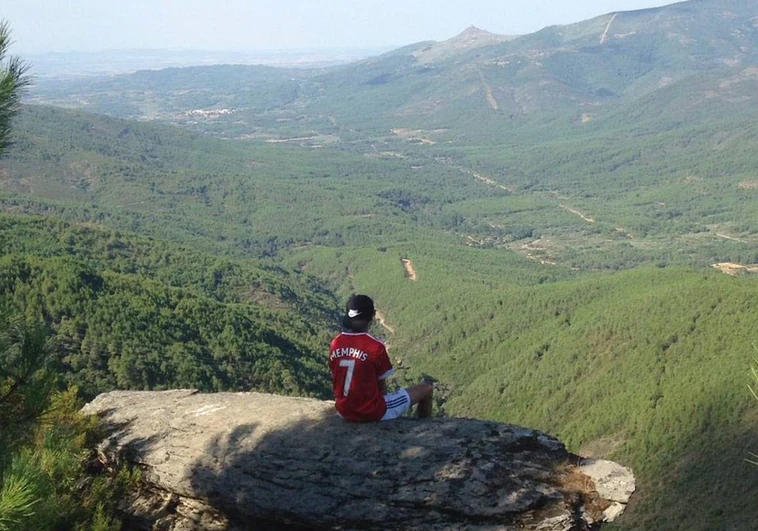 Paisaje repleto de árboles en la comarca cacereña de Sierra de Gata, con un joven sentado en la conocida como 'Piedra montá'.