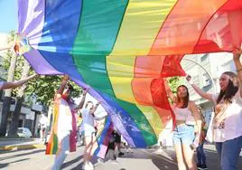 Un grupo de jóvenes sostienen una gran bandera arcoíris.