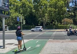 Una joven cirucla en patinete ante un cartel en el que se pueden ver los 42 grados.
