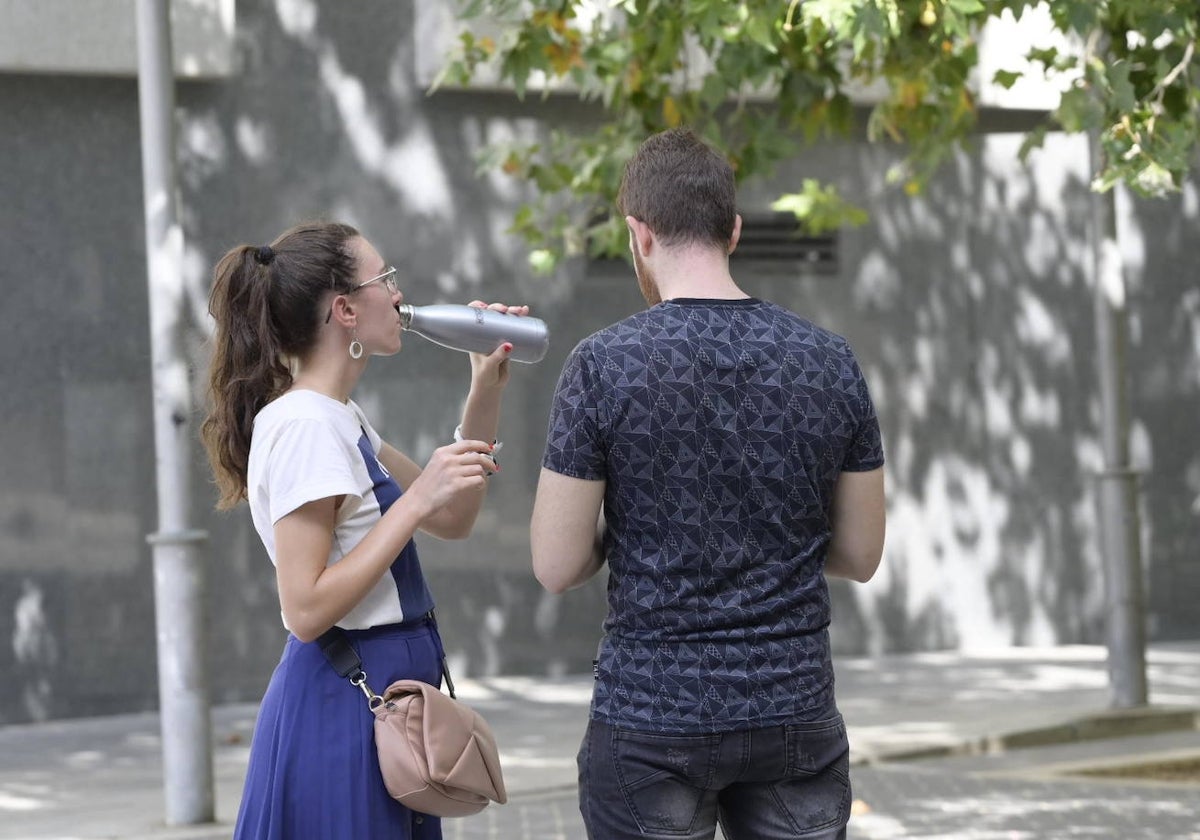 Una mujer bebe junto a un hombre en una zona de sombra, esta mañana, en Badajoz.