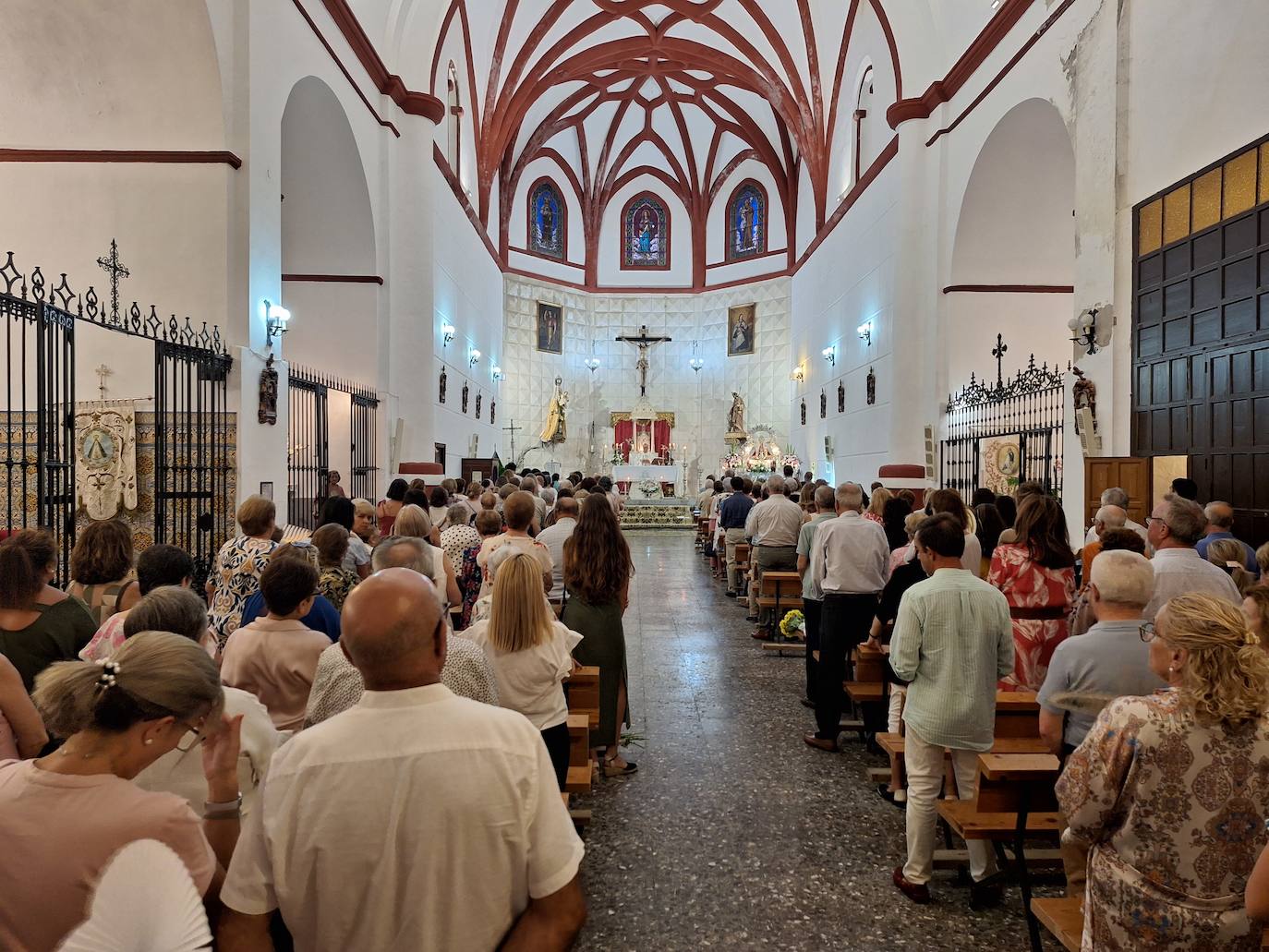 Imagen secundaria 1 - Arriba, imagen de la Virgen de la Luz con las flores ofrecidas por los fieles. Abajo, asistentes a la misa en la parroquia, y posterior degustación de pizzas y tortitas de tagarninas.