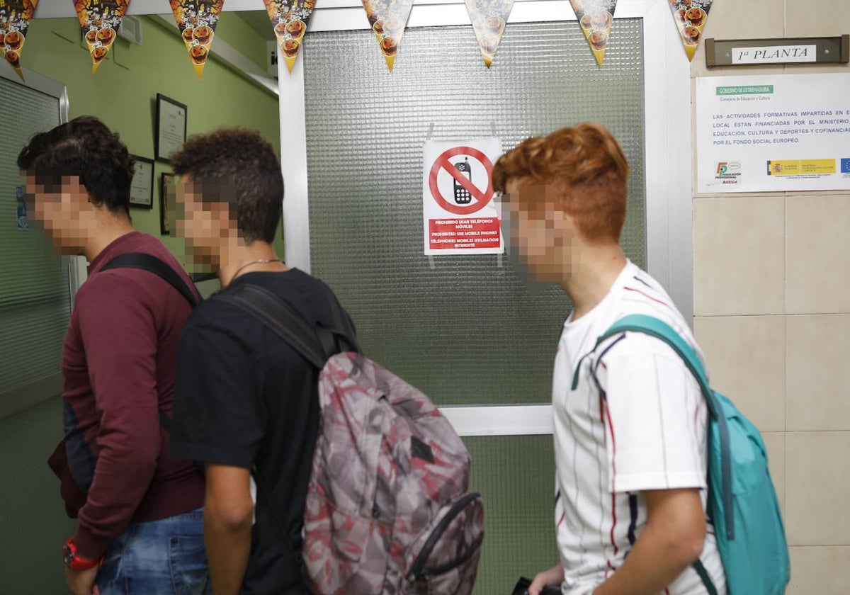 Alumnos del instituto Ágora de Cáceres pasan junto a un aula en la que hay un cartel que prohíbe el uso de teléfonos móviles.