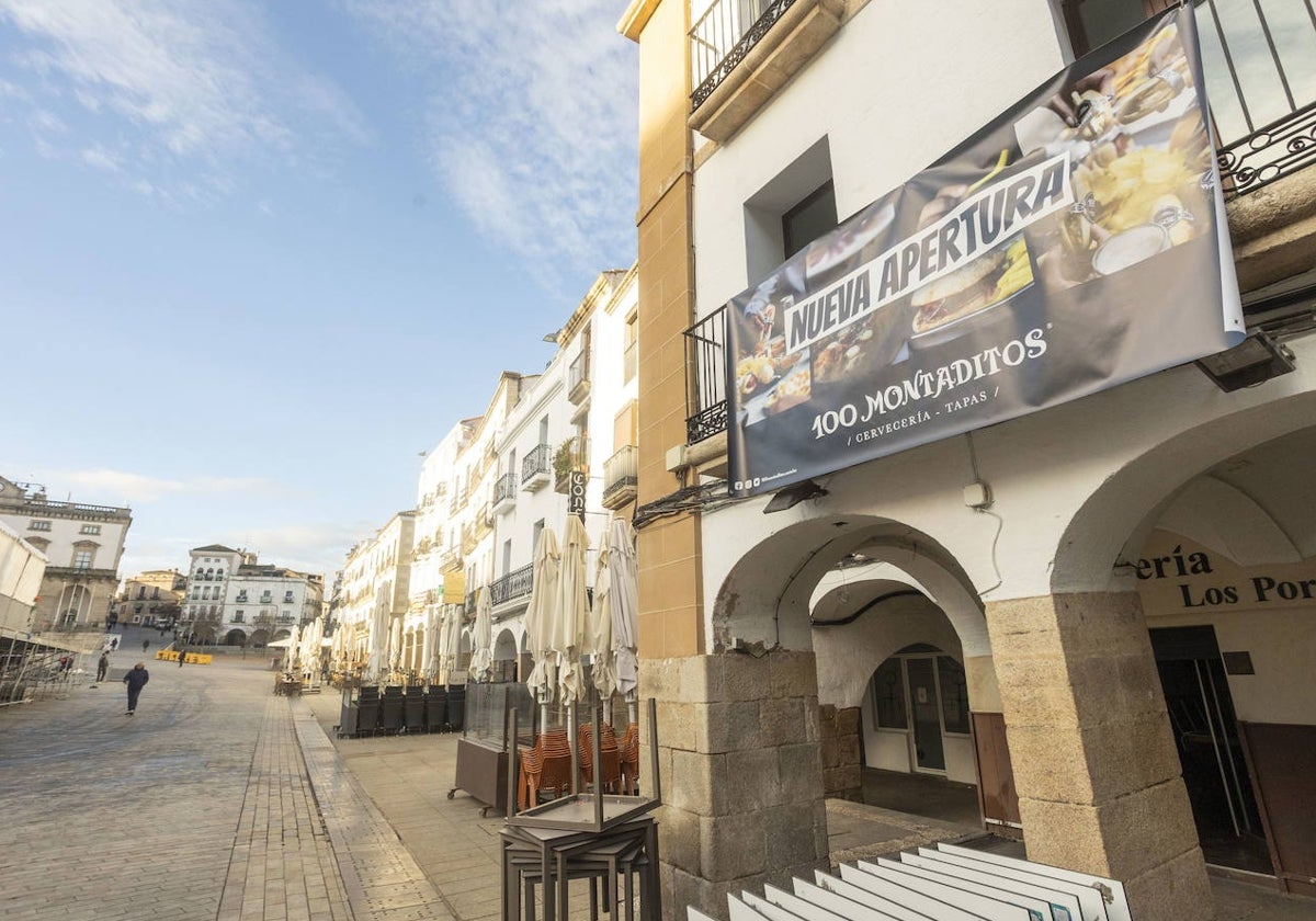 Una lona anuncia la apertura de la franquicia de hostelería en el local que ha dejado vacante 'Los Portales', en la parte baja de la Plaza Mayor de Cáceres.