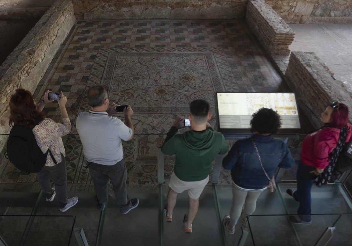 Varios turistas hacen fotos a un mosaico en la Casa del Anfiteatro de Mérida.