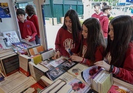 Alumnas de la Compañía de María consultan libros en una de las casetas de la feria instalada en el paseo de San Francisco este viernes en Badajoz.