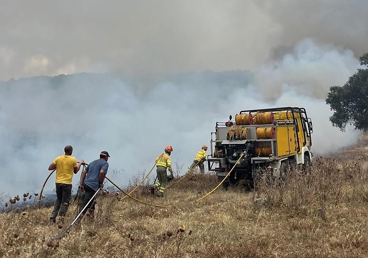 Imagen principal - Arriba, bomberos y vecinos voluntarios, haciendo labores de extinción terrestres en la finca más afectada. Abajo, varios vecinos de Alconchel, sofocando otro foco aislado junto a la carretera.