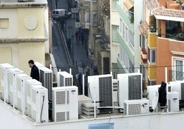 Un técnico revisa una instalación de aparatos de aire acondicionados en una azotea de pisos.