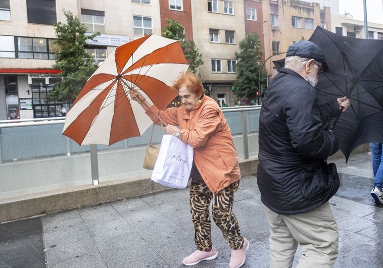 Dos personas agarran fuerte sus paraguas ante el viento en la ciudad de Cáceres. Vídeo: Fuerte aguacero en Badajoz a las 12.20 horas del miércoles.