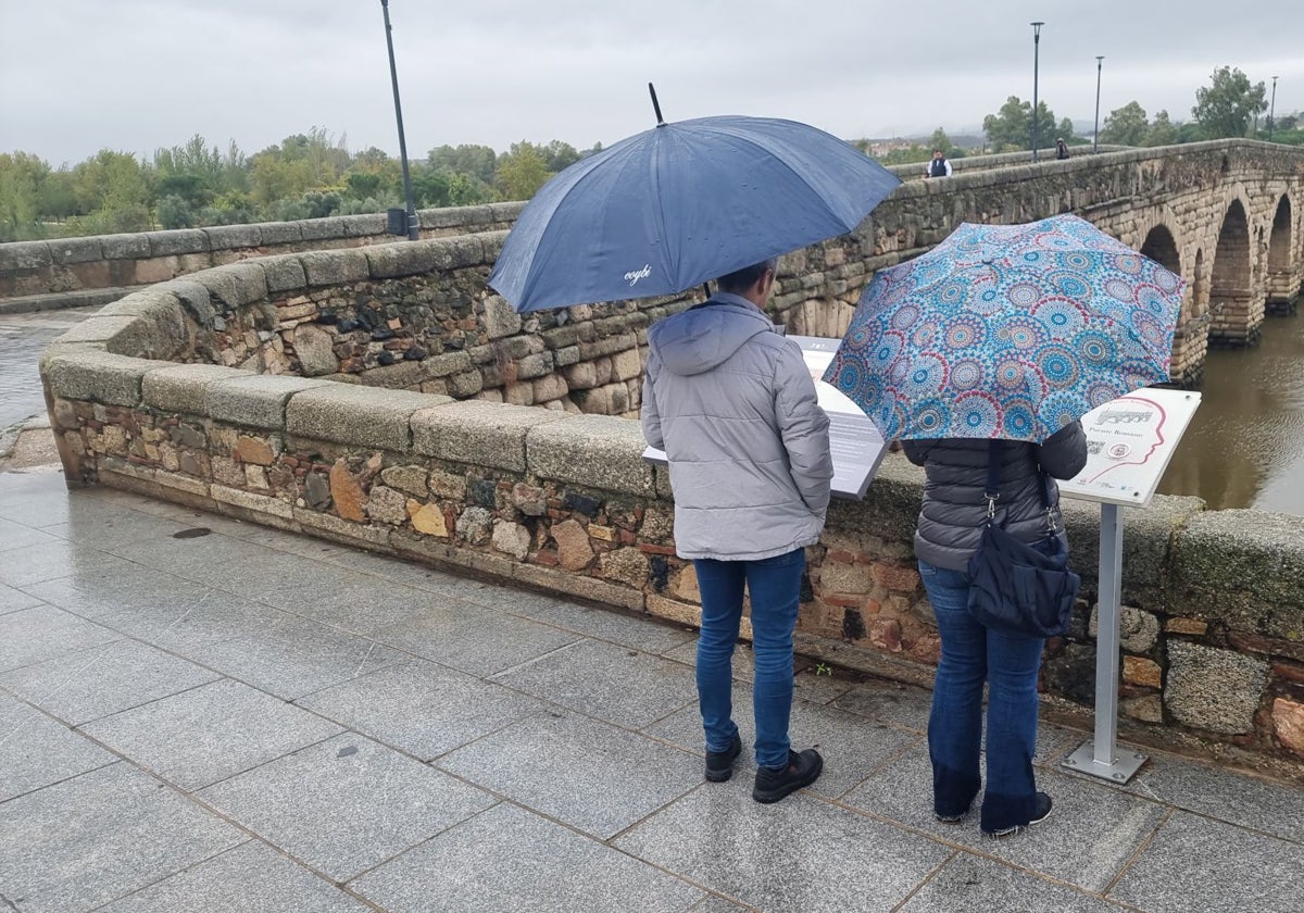 Dos turistas, la pasada semana, junto al Puente Romano de Mérida en una jornada lluviosa.