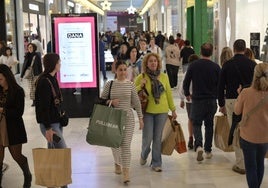 Clientes del centro comercial El Faro cargados con bolsas tras hacer compras.