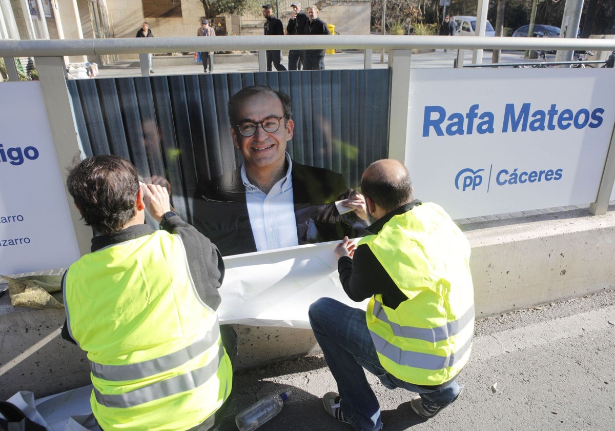 Dos operarios colocan un cartel de Rafael Mateos en el centro de Cáceres en la campaña electoral de 2023.