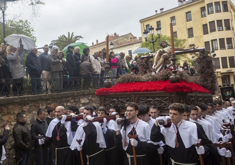 Momento en el que la cofradía de los Estudiantes pasa por la plaza de la Concepción con la imagen del Cristo del Calvario este Viernes Santo con algunos paraguas abiertos entre los asistentes.