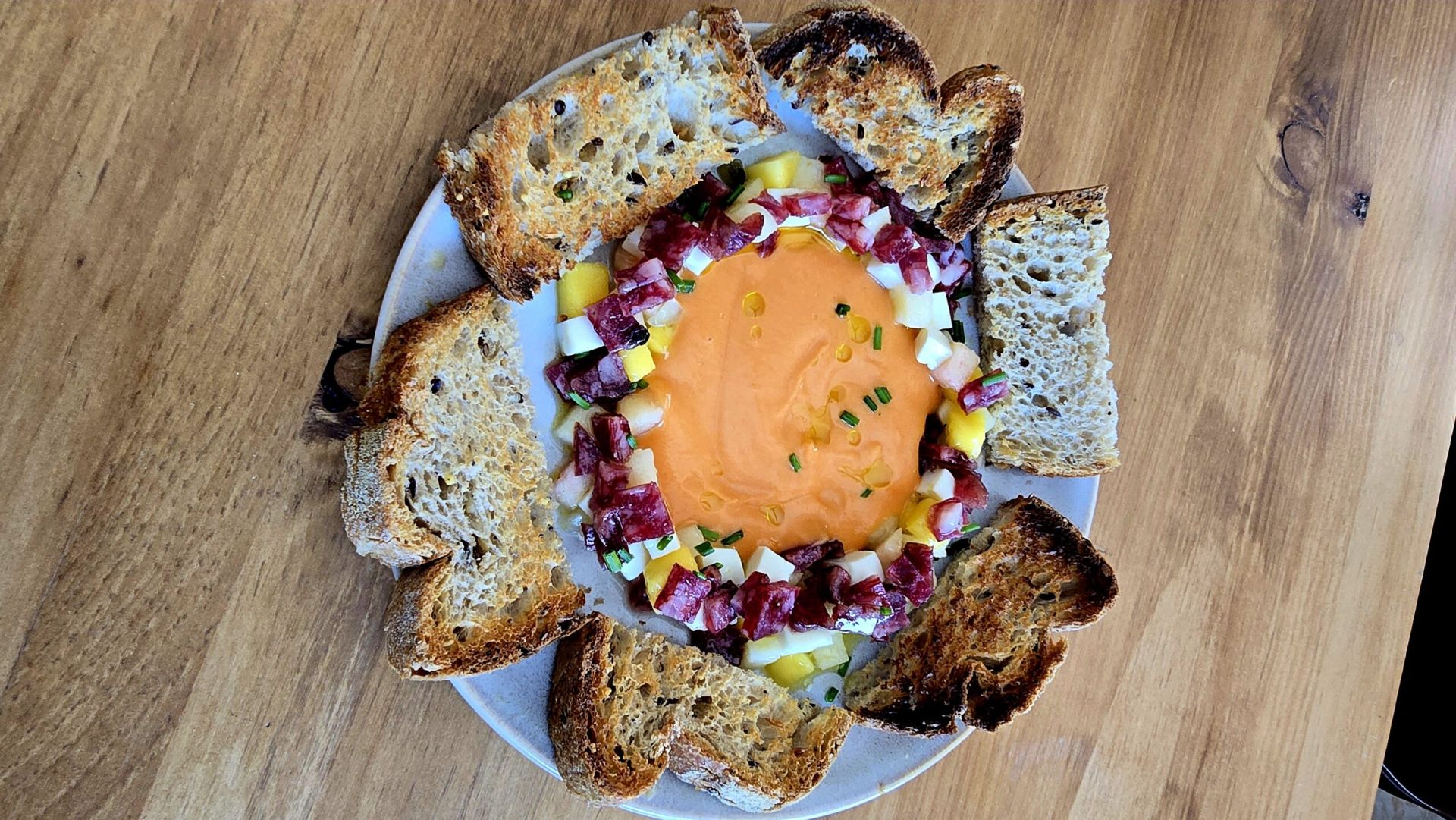 Tartar de fruta de temporada queso fresco y salchichon iberico de bellota con Salmorejo . Pan ecológico de masa madre, semillas, centeno y trigo , con posibilidad de pan sin gluten también. Para comerlo se puede mezclar con la cuchara y poner encima del pan tostado. O comerlo por partes