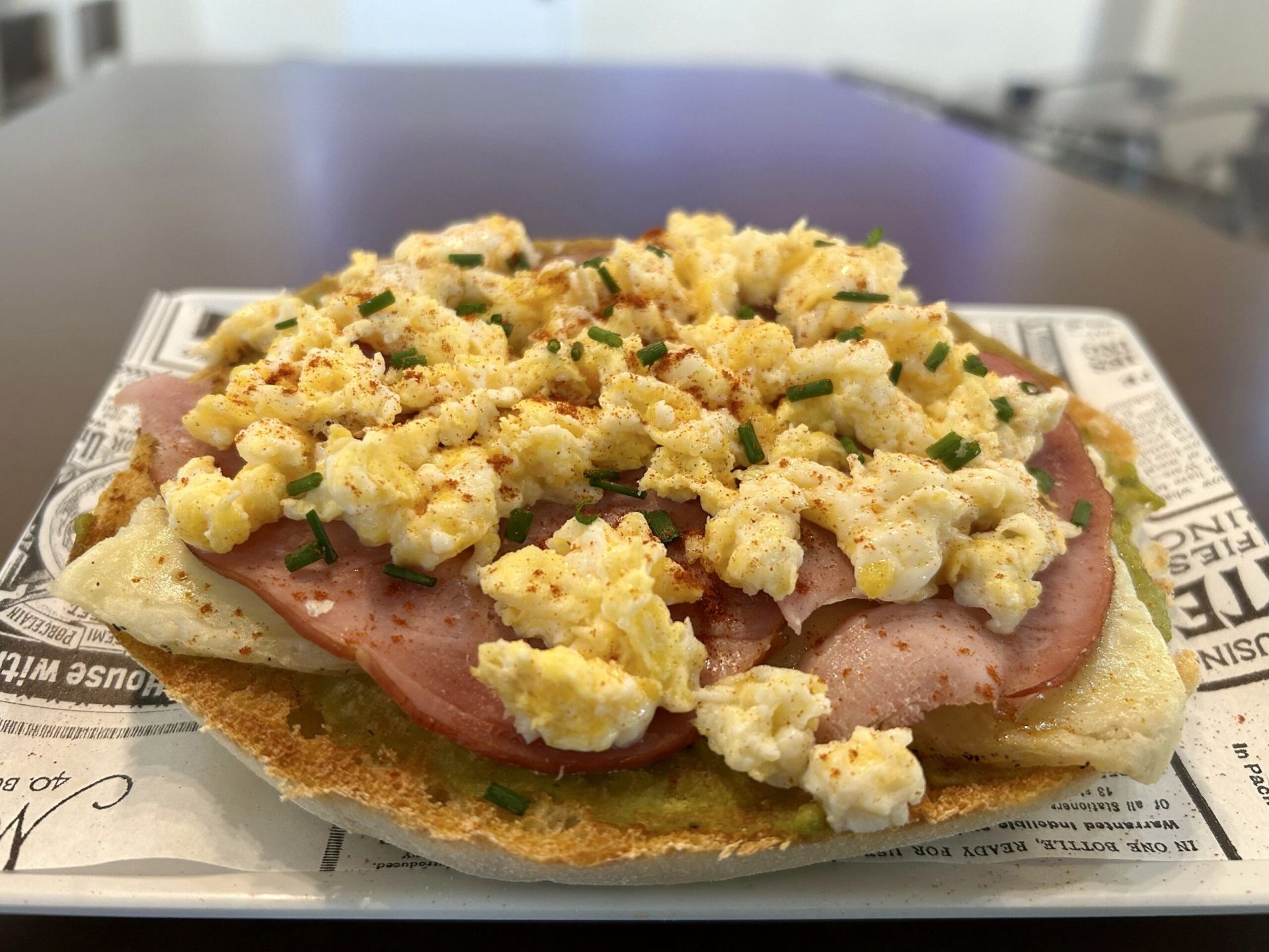 Esta tostada es una explosión de sabor y textura. Sobre una base de pan artesanal, se extiende un cremoso guacamole. Luego, se añade unas lonchas de queso manchego con un suave toque de trufa y finas lonchas de lacón. Coronando todo, un esponjoso huevo revuelto, espolvoreado con fresco cebollino y una pizca de pimentón de la Vera dulce.