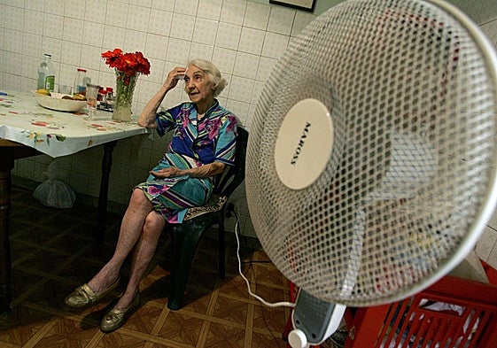 Una mujer mayor climatiza su casa con un ventilador.