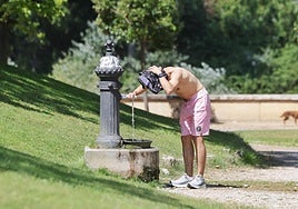 Un hombre se refresca en una fuente de un parque.