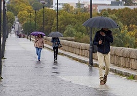 Tres personas cruzan con paraguas el Puente Romano durante el lluvioso abril, que dejó 77 litros.