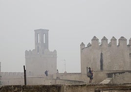 Turistas haciendo fotos este jueves en la Alcazaba de Badajoz, con la torre de Espantaperros envuelta en humo y bruma.