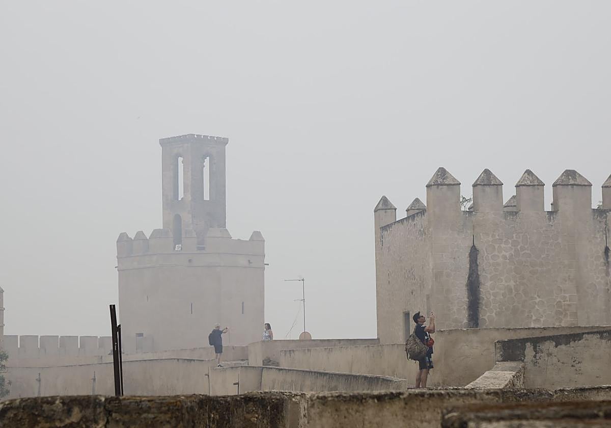 Turistas haciendo fotos este jueves en la Alcazaba de Badajoz, con la torre de Espantaperros envuelta en humo y bruma.