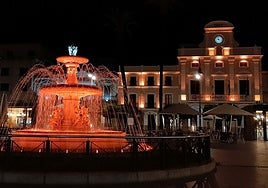Fuente de la plaza de España y fachada del Ayuntamiento, iluminadas con color naranja.