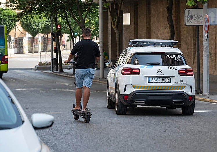 Un joven en patinete, sin casco, pasa junto al 'multacar'.