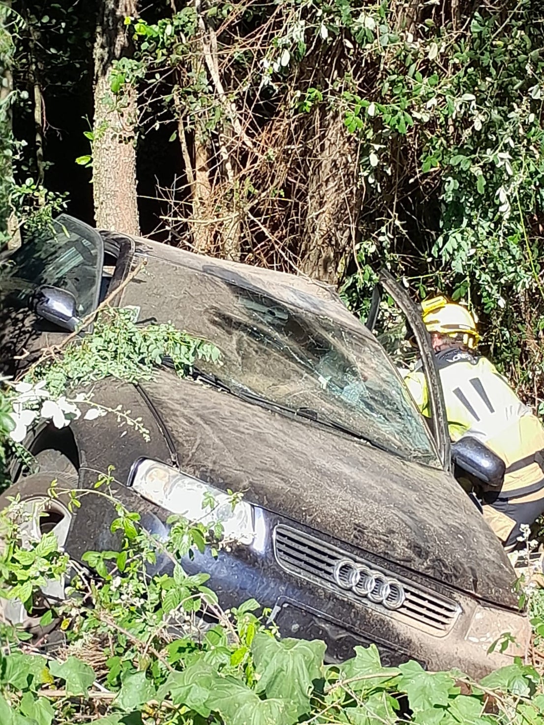 Los bomberos trabajan para rescatar a los dos ocupantes del turismo, que se ha salido de la vía y ha caído por un terraplén.