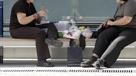 Dos mujeres comen sentadas en un banco. 