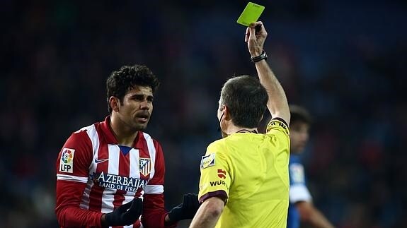 Un árbitro enseña la tarjeta amarilla a Diego Costa. 