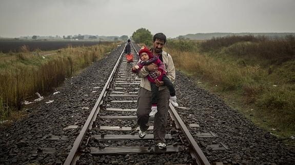 Un padre camina por las vías del tren, llevando a su hijo en brazos, unos cientos de metros después de haber cruzado la frontera entre Serbia y Hungria, entrando en la localidad de Roszke.