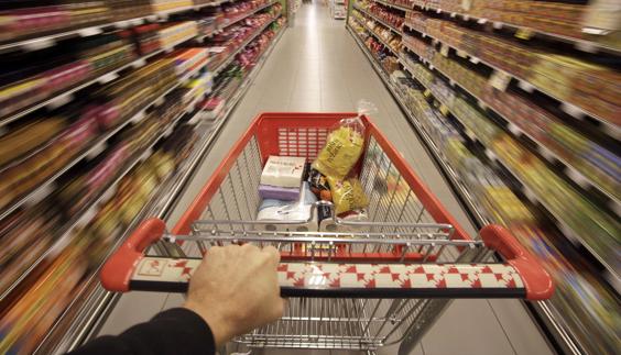 Un cliente conduce una carro de la compra a través de los pasillos de un supermercado.