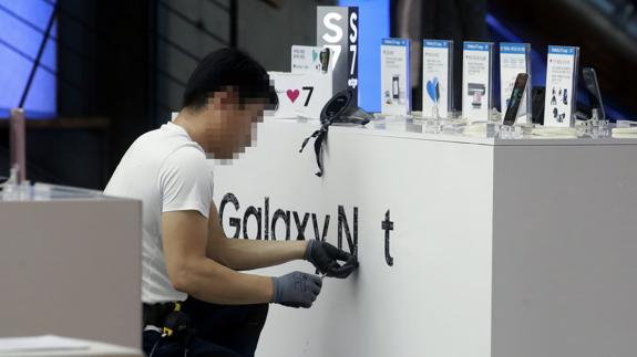 Un empleado quita las marca de Galaxy Note 7 en una tienda en Seúl.