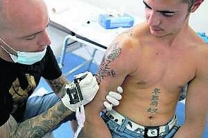 Tomás, del establecimiento 'Triángulo' de Badajoz, tatúa el brazo de un joven este verano. /ALFONSO