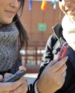 Dos alumnas pacenses usan sus teléfonos móviles en la puerta de su instituto. ::                             J. V. ARNELAS