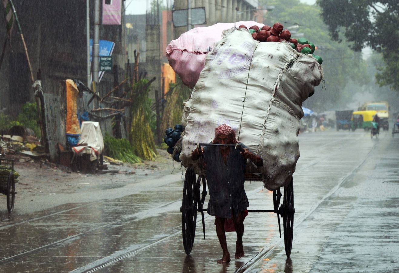 Un conductor de rickshaw indio transporta mercancías a lo largo de una carretera bajo una intensa lluvia en Calcuta.