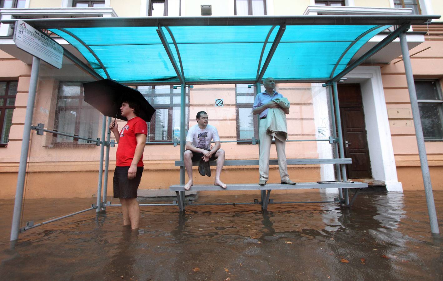 La gente espera el autobús en una parada inundada durante las lluvias en Minsk.