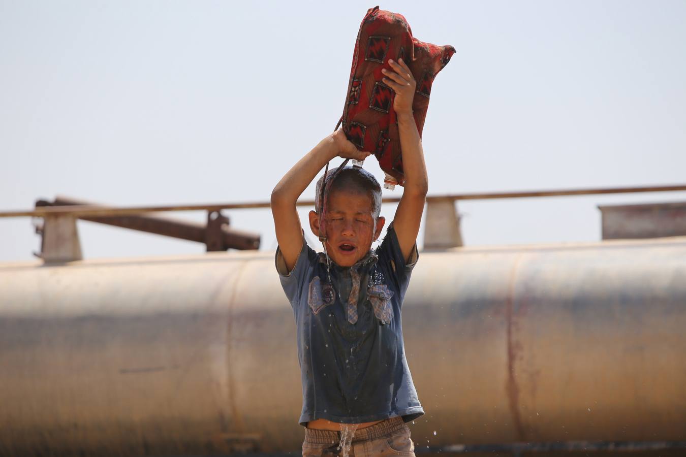 Un joven refugiado iraquí, vierte el agua sobre sí mismo en el campamento de Newroz en la provincia de Hasaka.